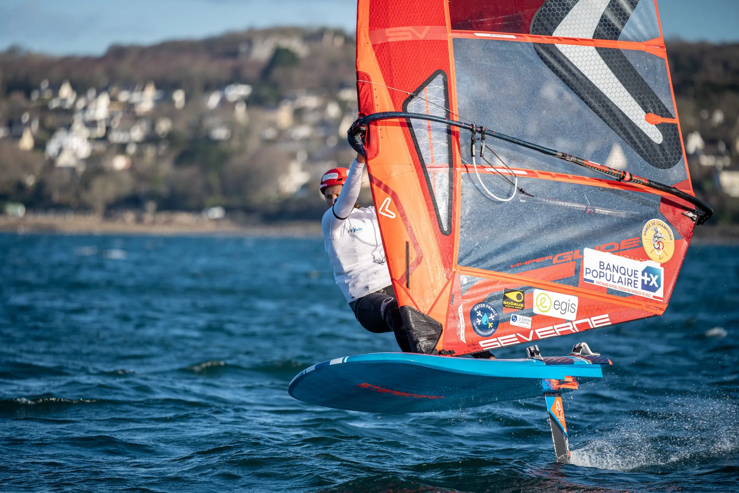 A windsurfer with a sail, flying above the water on a foil board