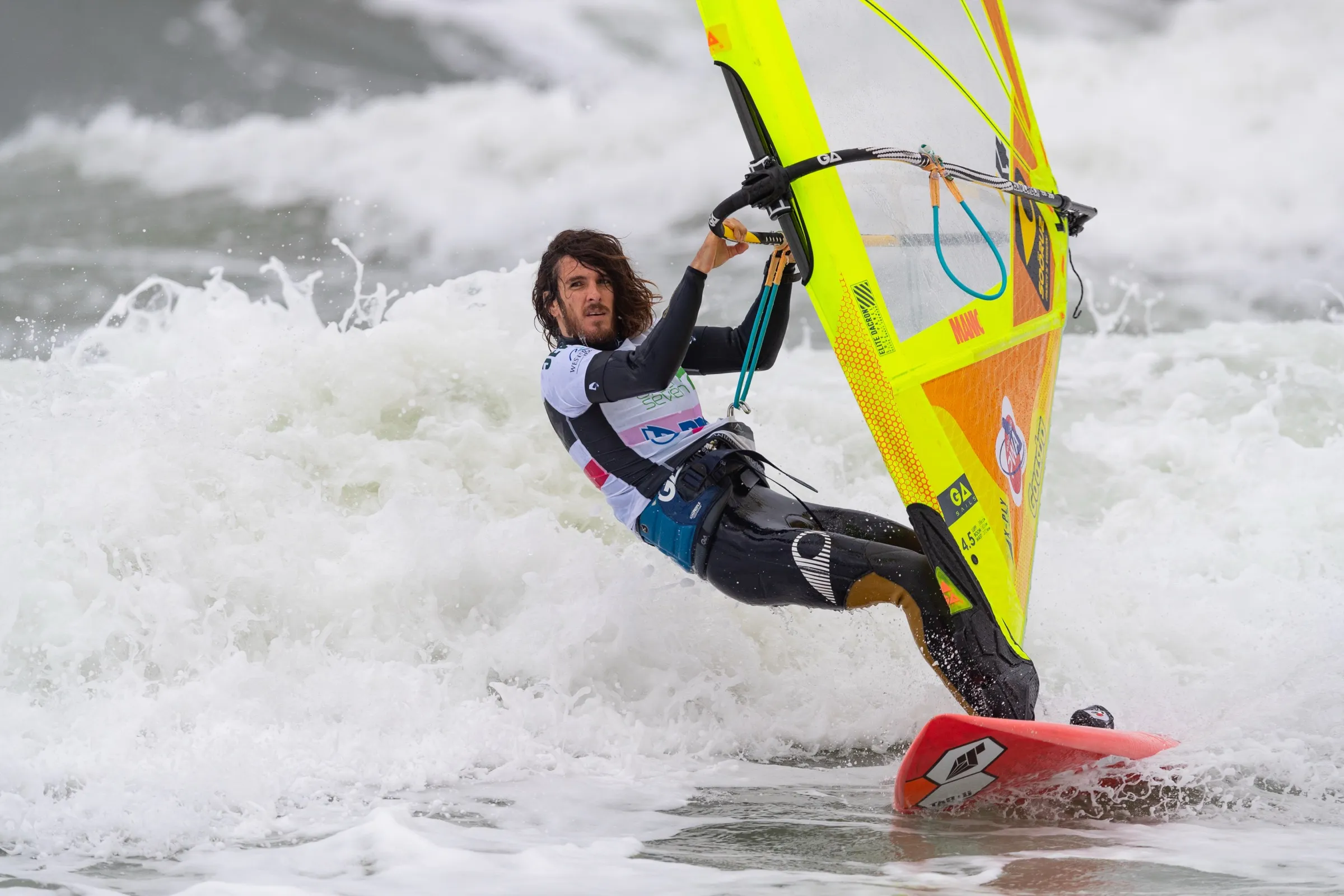 Ein Windsurfer mit gelbem Segel dreht auf einer Welle