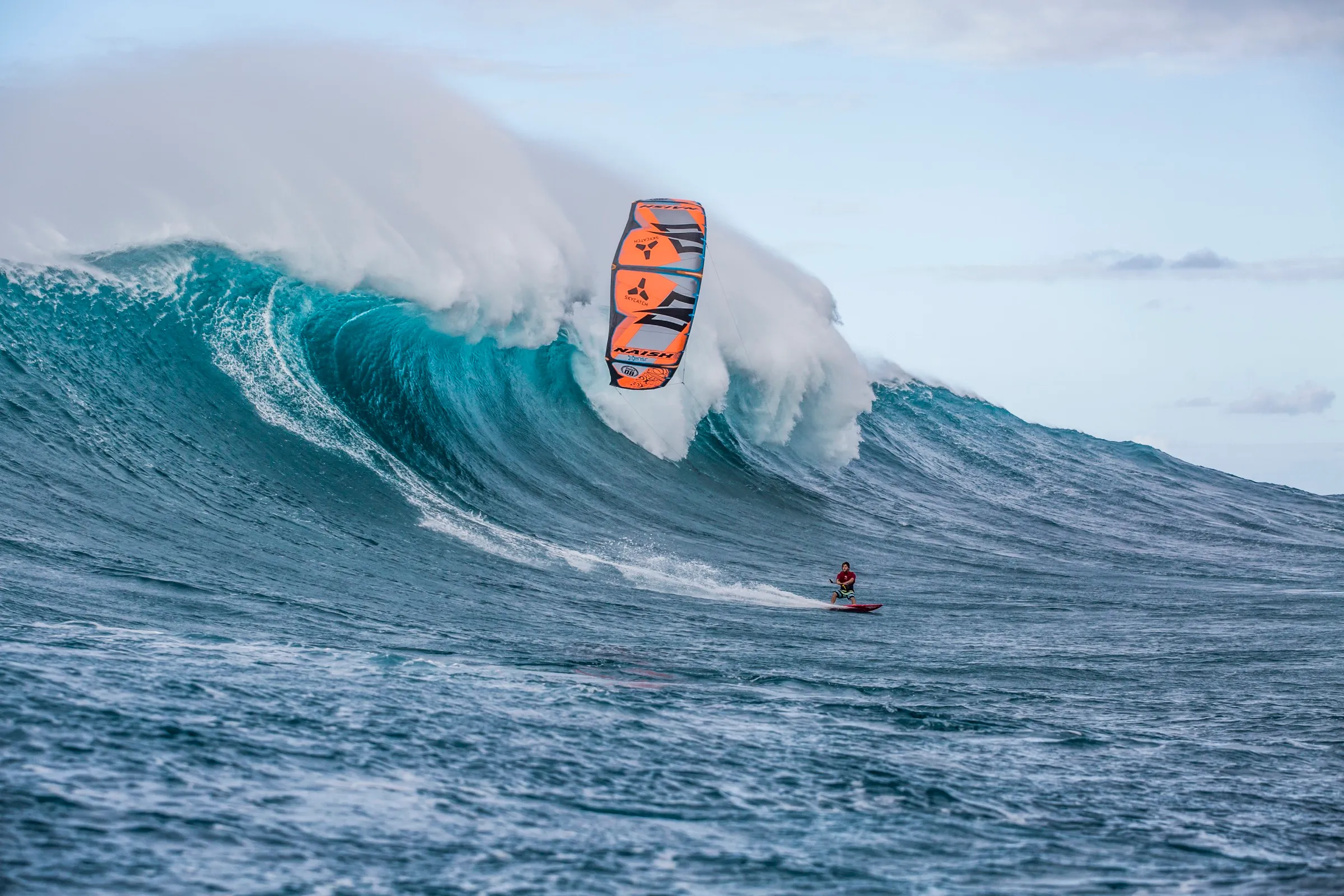 A kitesurfer riding down the face of a huge breaking wave