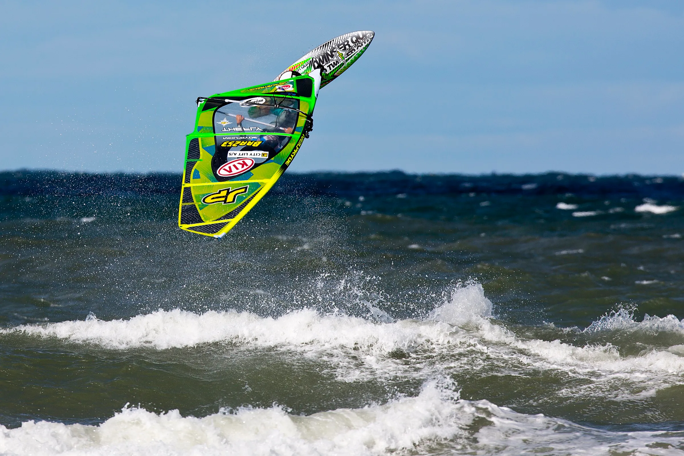 Ein Windsurfer mit grünem Segel kopfüber in der Luft über dem Meer