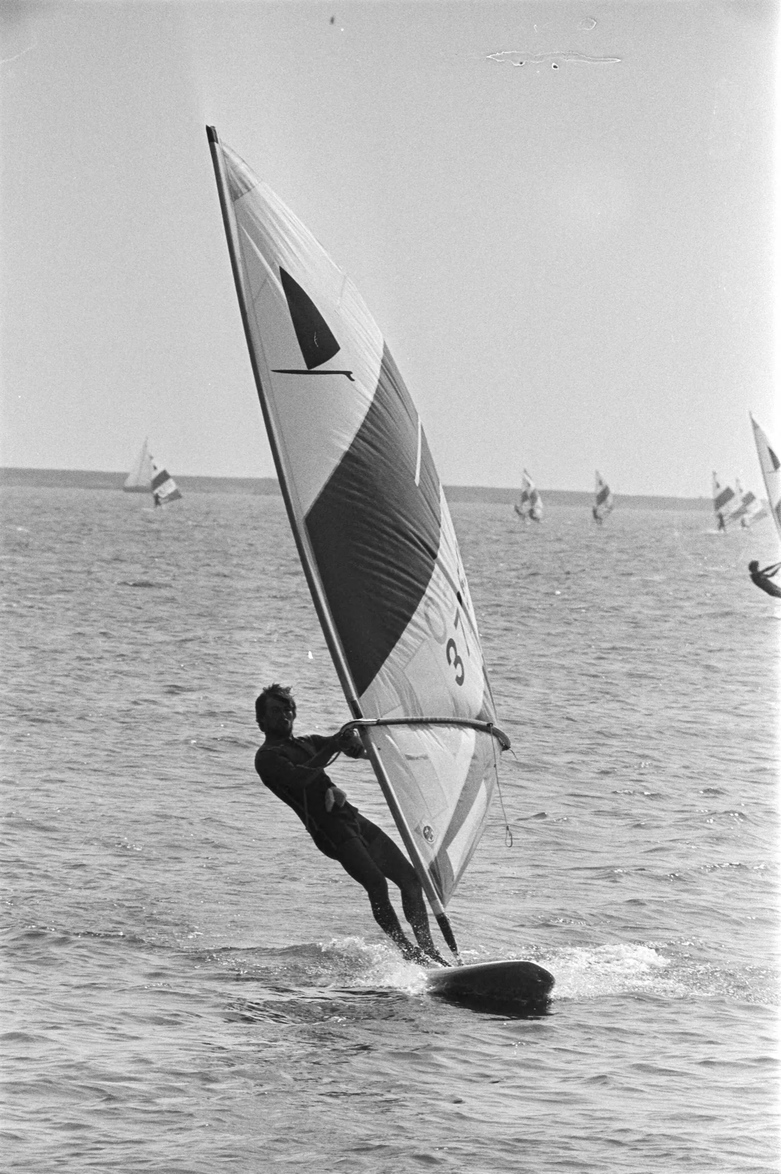 Windsurfers with striped sails racing close together on a lake