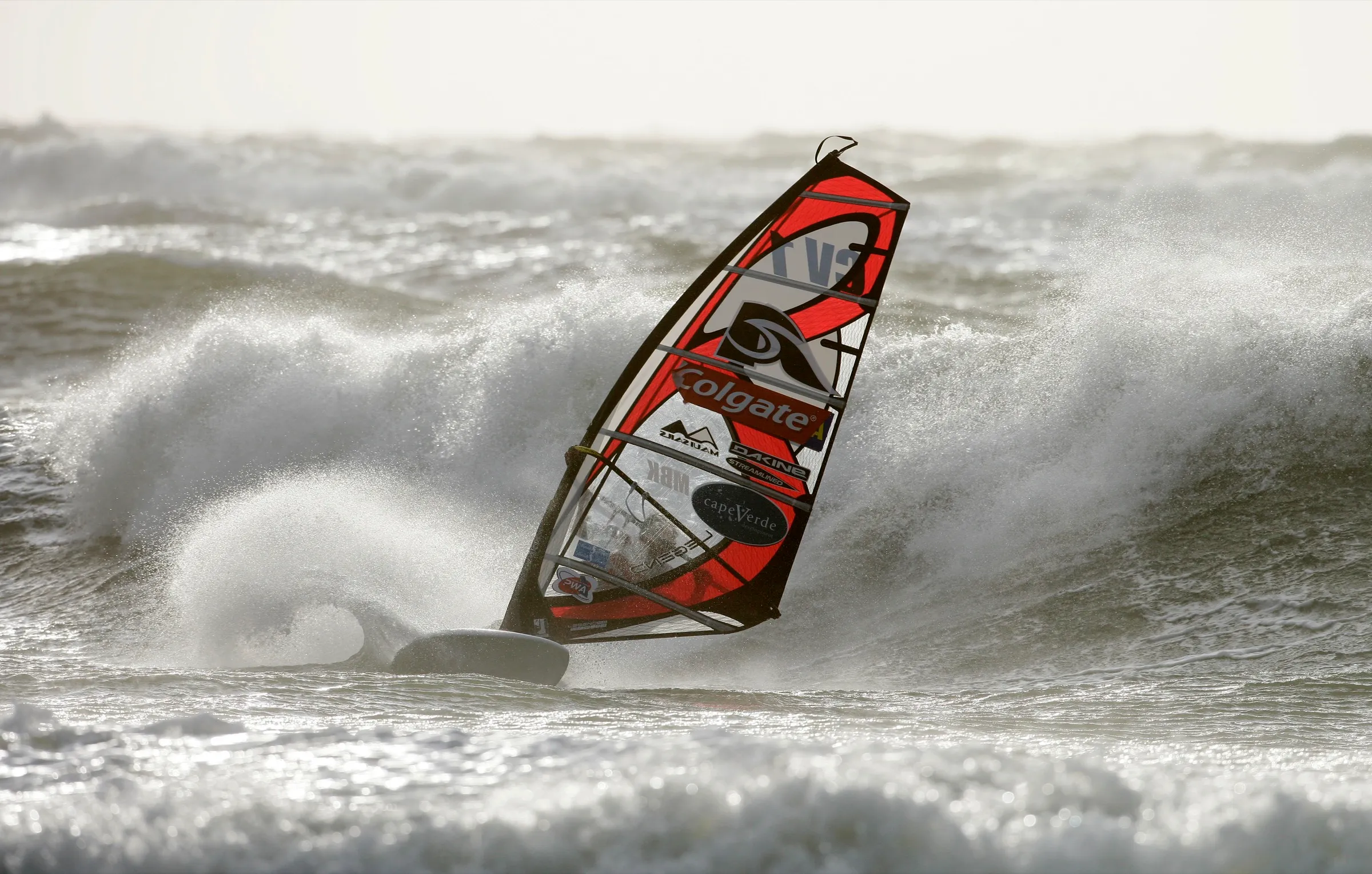 Ein Windsurfer mit rotem Segel fährt durch das Weißwasser