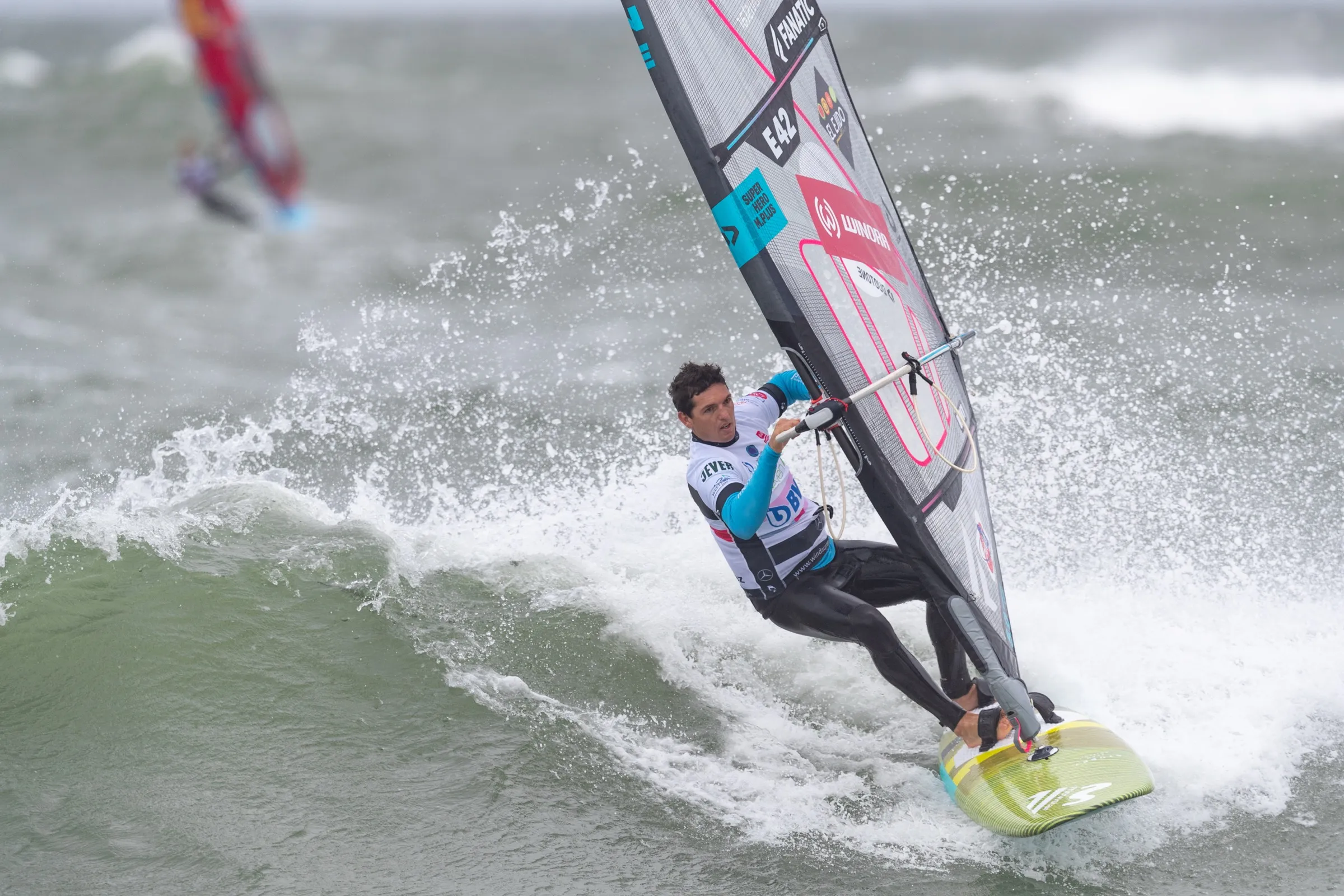 A windsurfer with a white sail turning on a wave