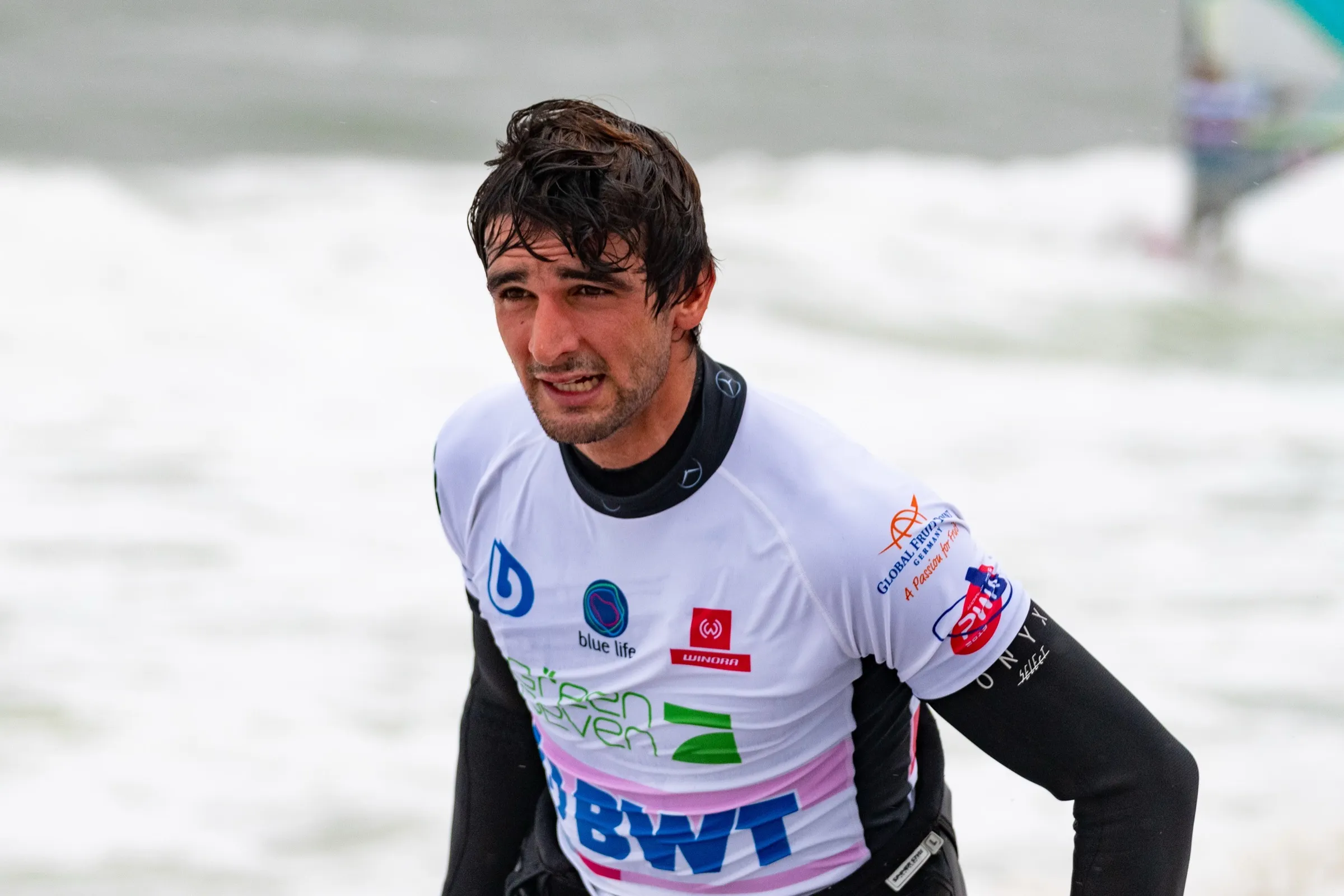 Marc Paré in a wetsuit and contest vest on the beach, smiling