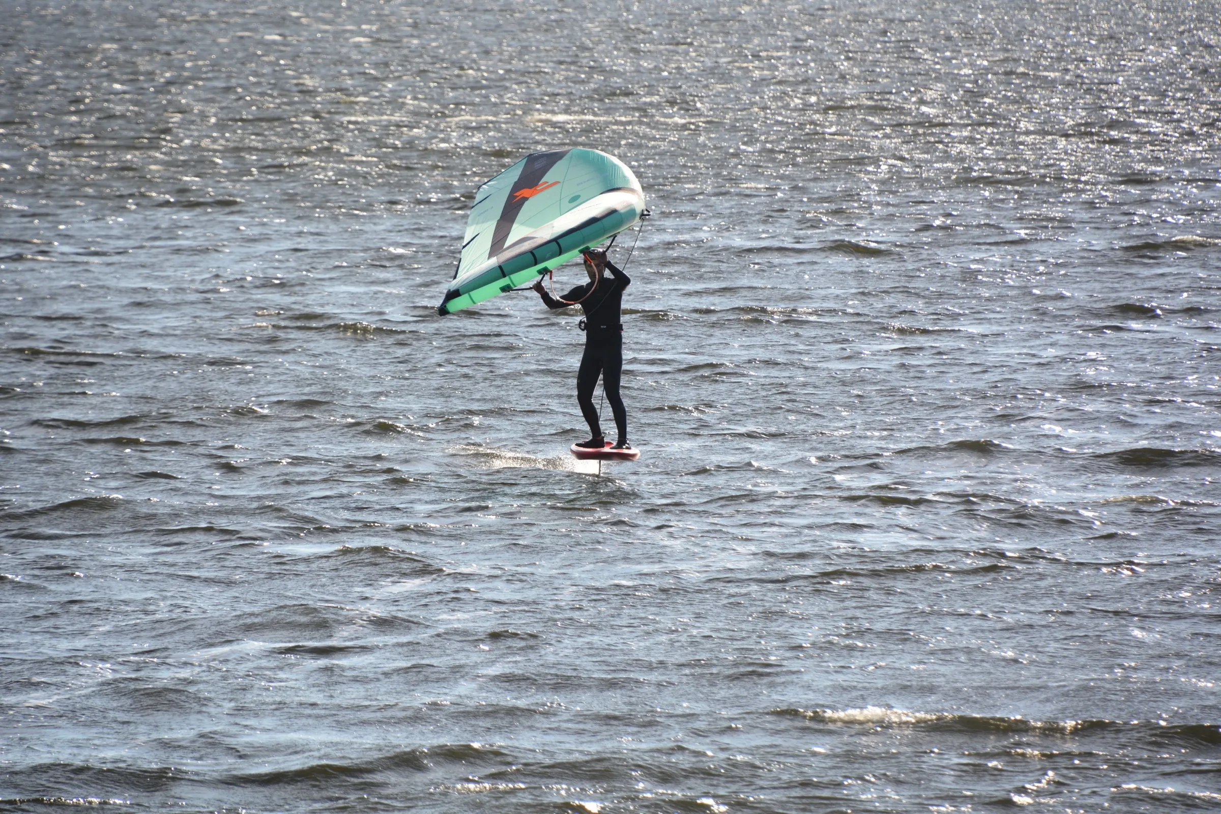 A wing foiler holding an inflatable wing above a foil board