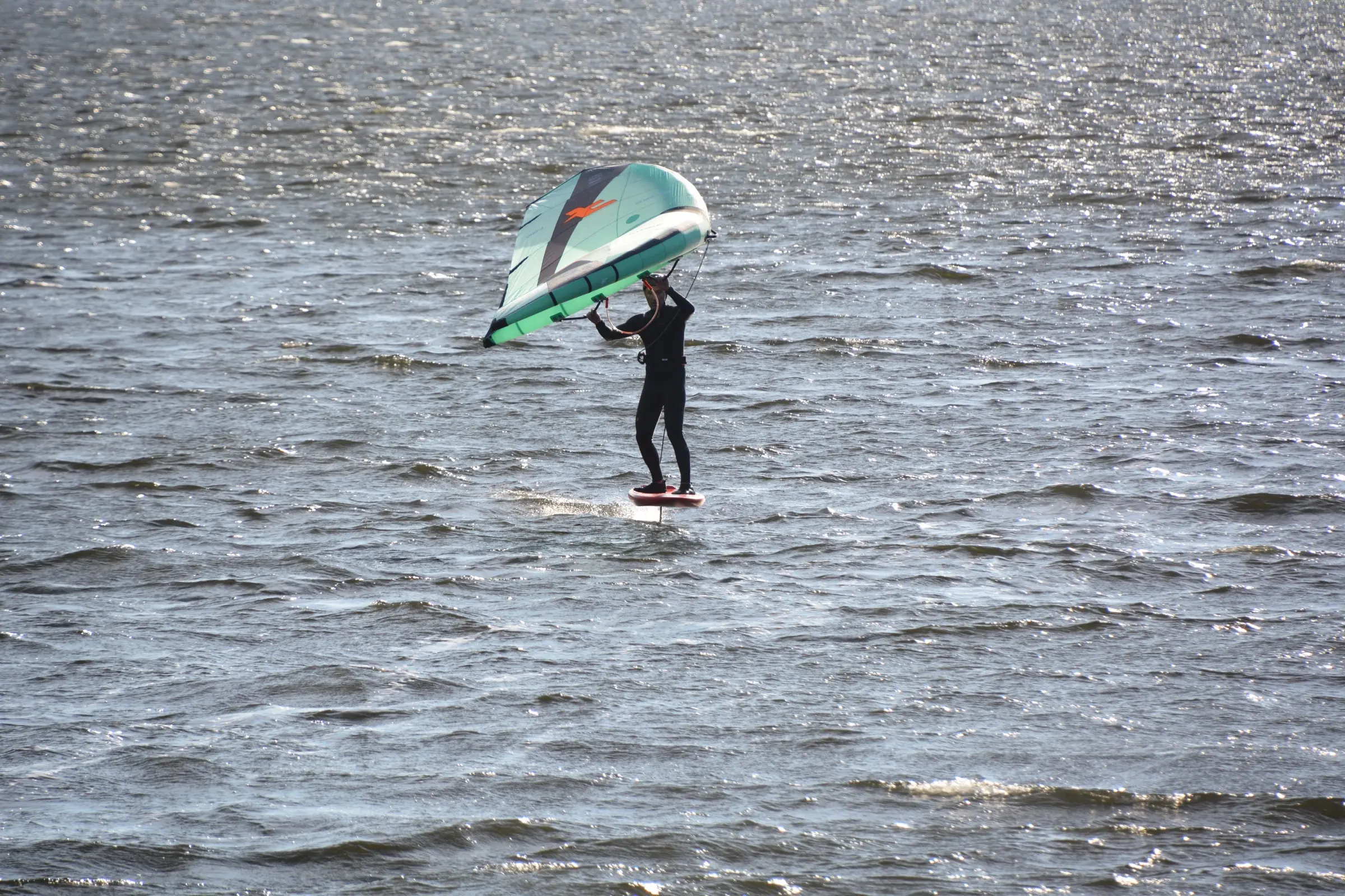 A wing foiler holding an inflatable wing above a foil board
