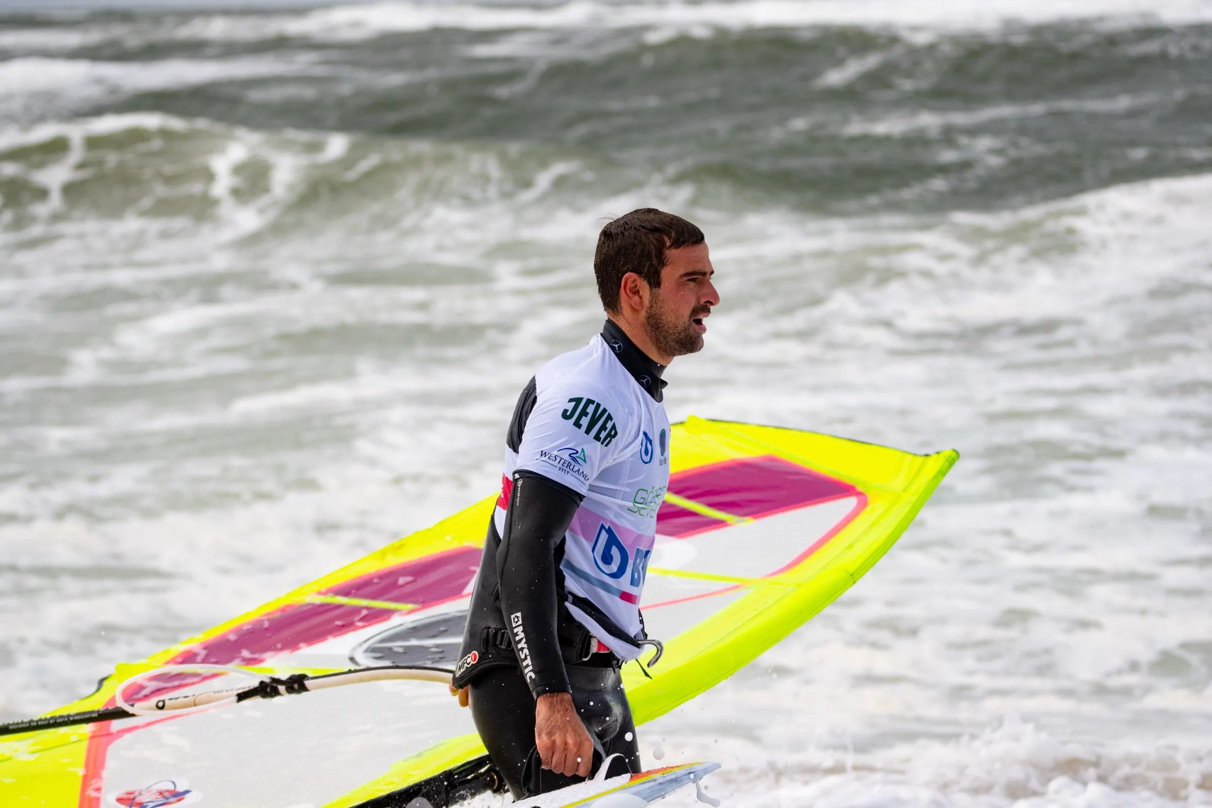 Marcilio Browne carrying his board and sail through the shallows