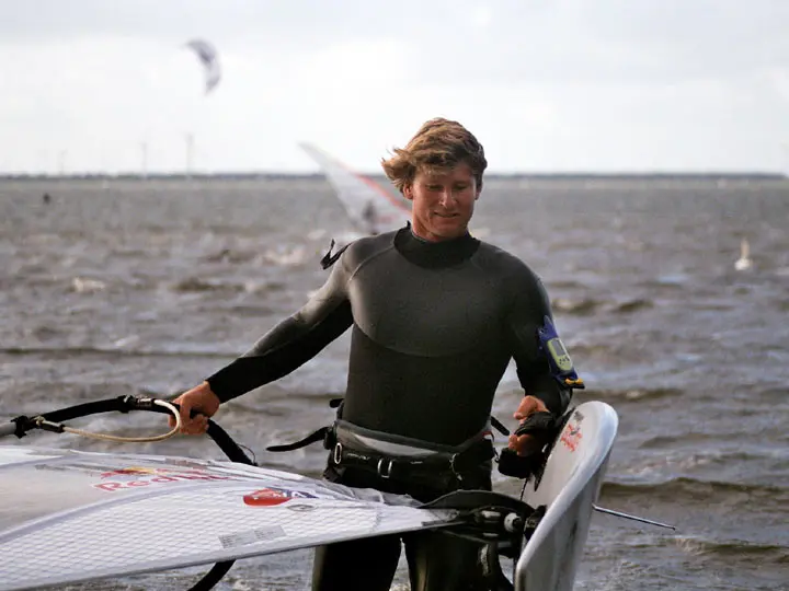 Björn Dunkerbeck in a wetsuit on the beach, holding his board and rig