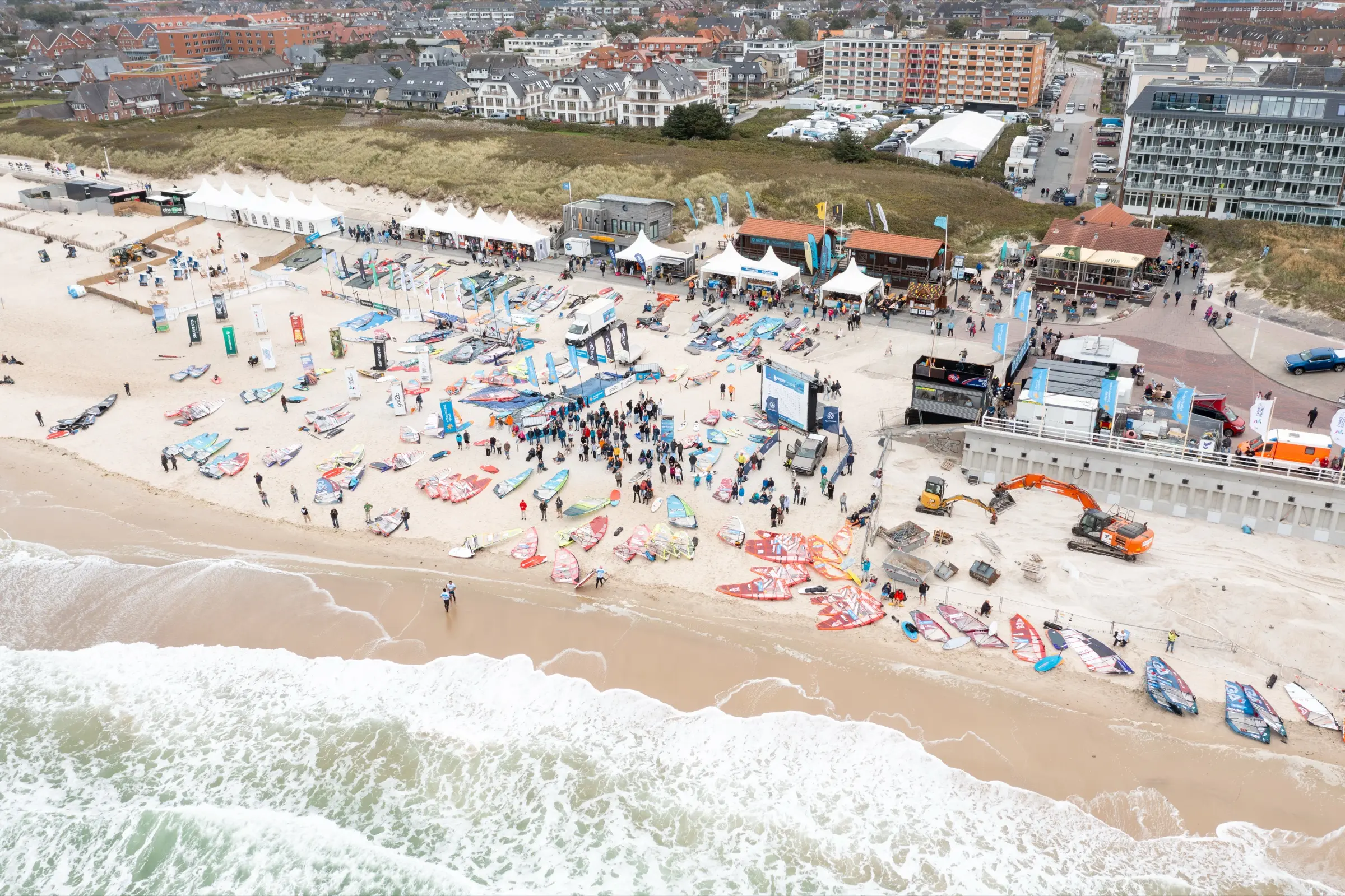 Aerial view of a beach full of windsurf rigs, tents and spectators
